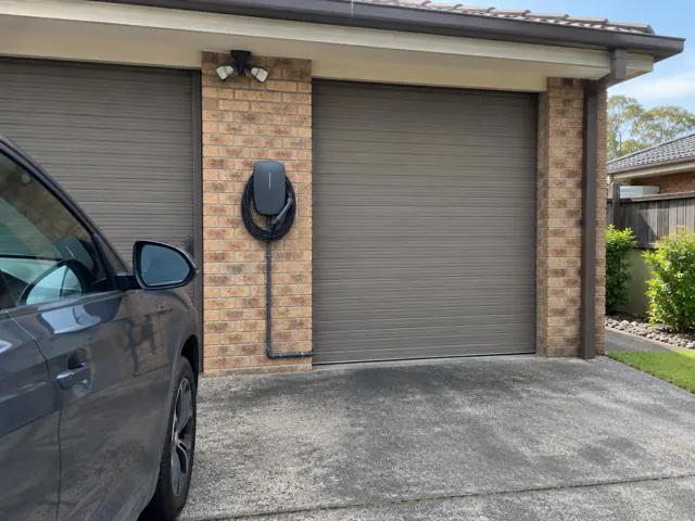Wall-mounted EV charger on a brick garage wall beside a driveway in Belmont North