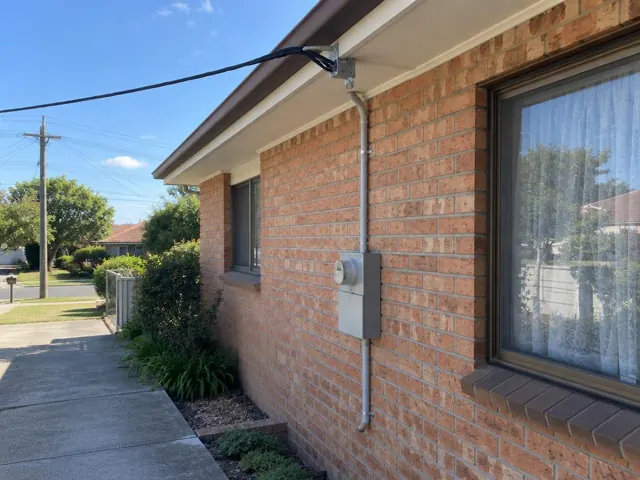 Overhead service cable and point-of-attachment bracket on a brick house exterior in Jewells